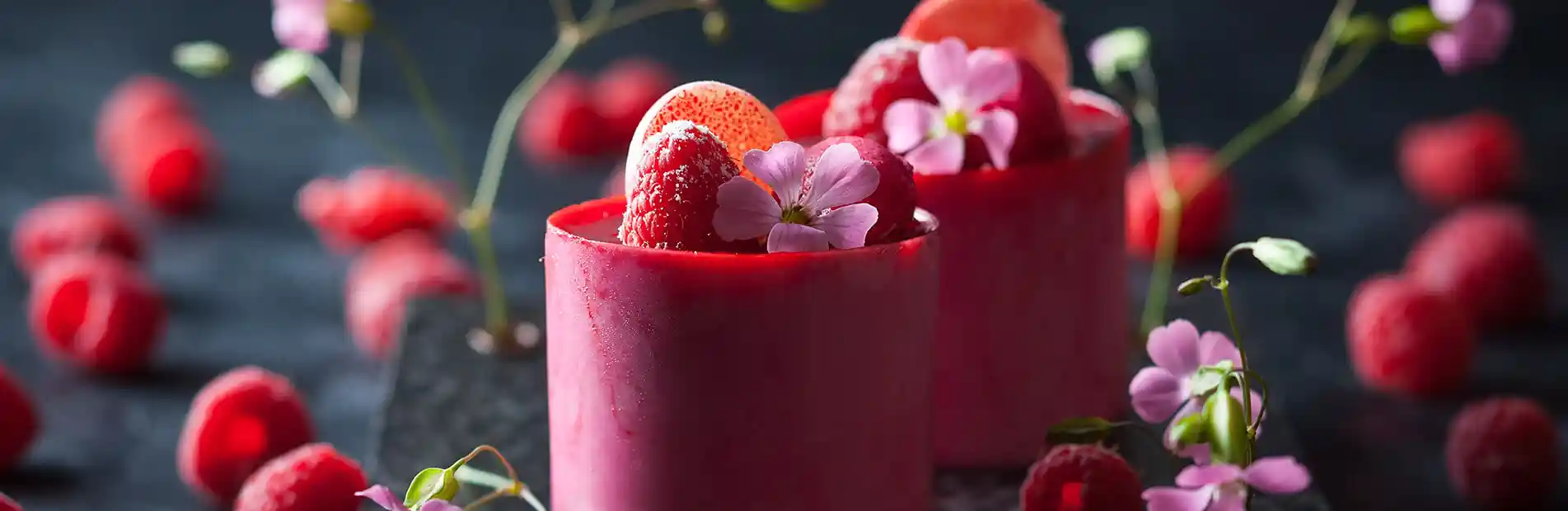 A refreshing raspberry beverage served in a tall glass with ice cubes, showcasing vibrant red hues and garnished with fresh raspberries on the rim